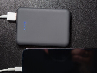 Power bank for charging mobile devices on a black background. Smartphone charger with power supply. External battery for mobile devices.