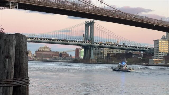 New York, USA - 2023: NYPD police boat at Brooklyn Bridge and panoramic sunset view of downtown Manhattan after sunset. NYPD boat responding to emergency on the East River, NYC.
