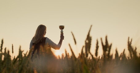 Silhouette of a woman with a champion cup in a field of wheat