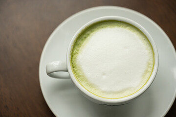 Top view white cup of hot green tea latte on wood background in restaurant.Top view with copyspace for your text.