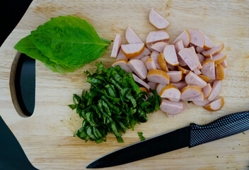 Sliced sausage and chopped basil leaves on a cutting board