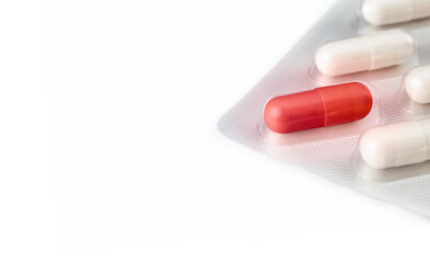 Red pill capsule in blister package medication. Pill pack dispenser with cream capsule. Concept for substance abuse, addiction, prescription drugs, supplements and vitamins. Selective focus. Isolated.