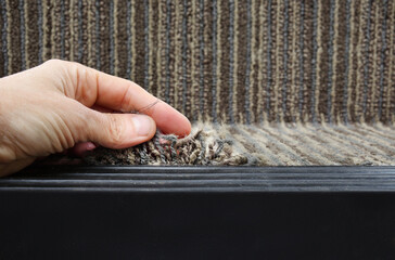 Person showing frayed carpet coming loose on stairstep, stair nosing or stair edging. High traffic staircase with commercial carpet damage by the edge, causing tripping hazard. Selective focus. - obrazy, fototapety, plakaty