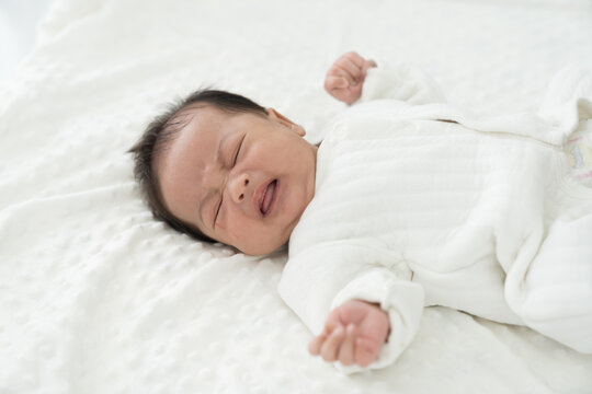 Newborn baby crying on blanket on white bed. Family, love and new life concept