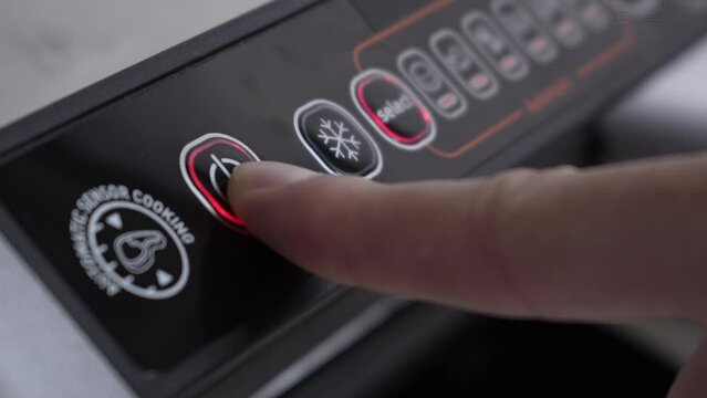 A man's finger presses the power button on a home electric grill to turn it off. Household electrical appliances in the home kitchen. Black electric grill control panel close-up.