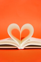 Open book with pages in heart shape on a bright orange background. Poetry Day. Read a book day. Knowledge day. Back to school minimal concept. Space for text. Teachers day. Copy space
