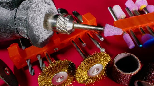Closeup pan shot of a small drill tool with multiple abrasive attachments by way of grinding stones, sandpaper and wire brushes.