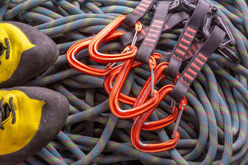 a pair of climbing shoes and a few climbing quickdraws on a background of flaked rope