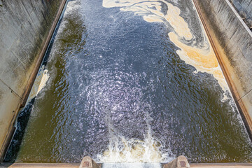 Water flowing from gate of Staumauer Bitburger dam into Prum rive, pollution with brown stain on...