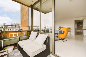 a balcony with white furniture and an orange chair on the right hand side, looking out to the city below