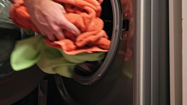 A man loads colored towels for washing into the drum of the washing machine.