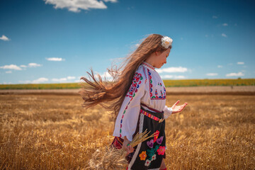 Girl in traditional ethnic folklore costume with Bulgarian embroidery standing on a harvest golden...