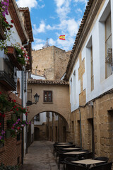 Fototapeta na wymiar Vista de una callejuela típica con arco y torre con la bandera de España en Baeza, Jaén, Andalucía, España.
