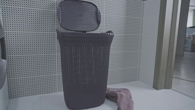 Bunch of dirty towels flies into spacious grey laundry basket in tiled bathroom. Soiled towels for cleaning with detergent in washing machine