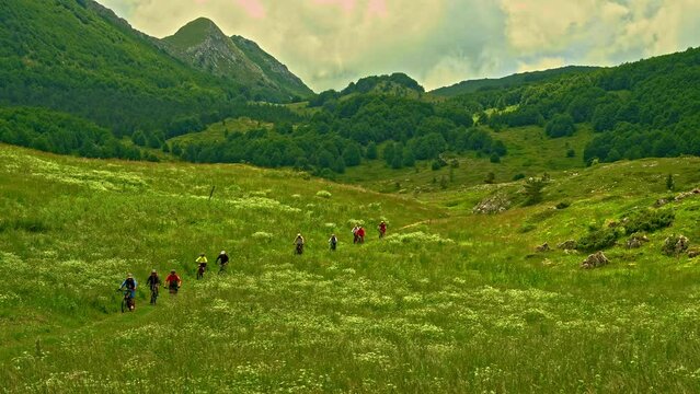 A group of bikers cross the meadow in one of the green valleys in the Gran Sasso and Monti della Laga National Park. Abruzzo, Italy, Europe