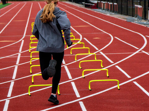 One female runner running over yellow mini hurdles in lane on a track