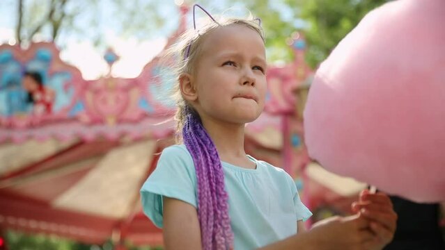 happy baby girl eating cotton candy at amusement Park in summer