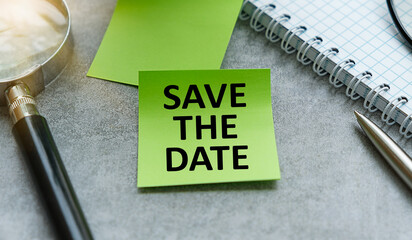 Save the date - concept of text on sticky note and pen on gray background