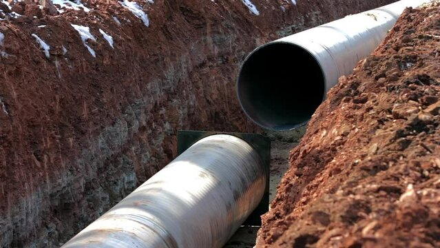 Two large gas pipes lie in a trench at the construction site of a new gas pipeline