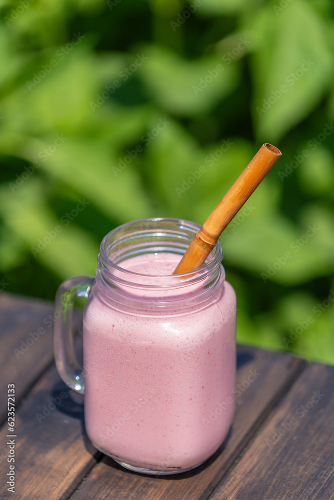 Wall mural fresh chilled strawberry smoothie in a glass mug on a wooden table on a sunny summer day, closeup. r