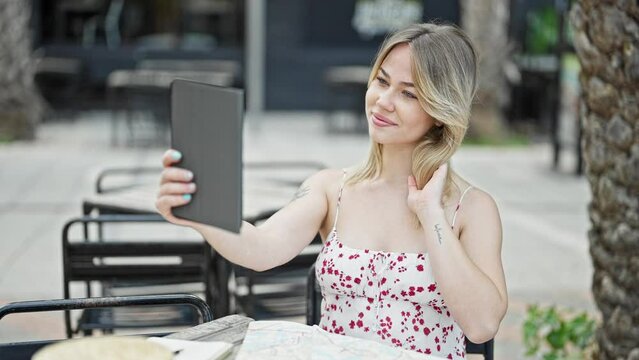Young blonde woman make selfie by touchpad sitting on table at coffee shop terrace