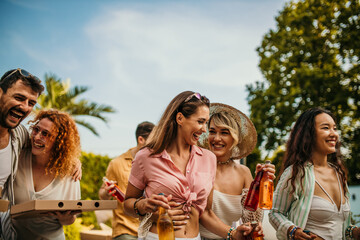 Gropu of people walking through the house yard, carrying a pizza and drinks, ready to have a house party.