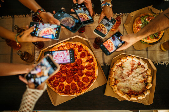 Friends gather in the living room, taking pictures of a pizza for social media.