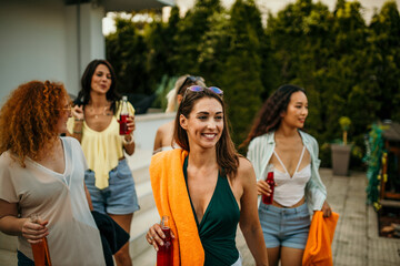 The group of friends arrives at the pool area, wearing their trendy swimwear and carrying beach towels, drinks and pool accessories.