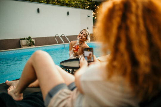 Two females by the poolside, striking a pose and capturing a photo with big smiles and playful poses.