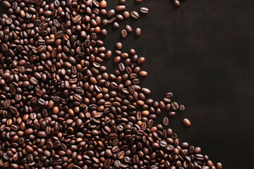 Roasted coffee beans on a wooden dark table, top view. Background of fragrant brown coffee beans scattered over the surface. copy space. Place for text
