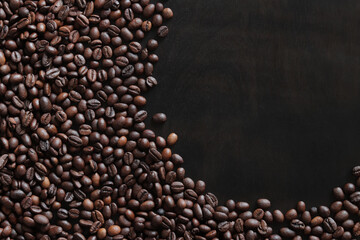 Roasted coffee beans on a wooden dark table, top view. Background of fragrant brown coffee beans scattered over the surface. copy space. Place for text