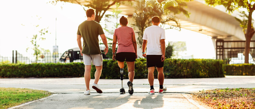 Friend support Friend with a prosthetic leg while exercising outdoor. People walking together on park outdoor. Exercise walking  woman with prosthetic leg and friend support together in  park outdoor