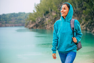 Beautiful woman traveler or tourist with backpack hiking in mountains near lake with beautiful summer landscape on background. Adventure, travel, holiday concept.