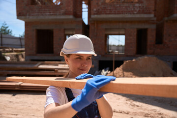 Woman building engineer bringing wooden girder, working at roof construction