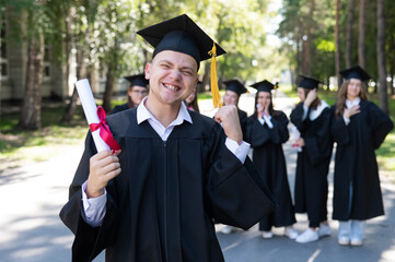 Happy young caucasian man celebrating graduation. Crowd of students graduates outdoors.