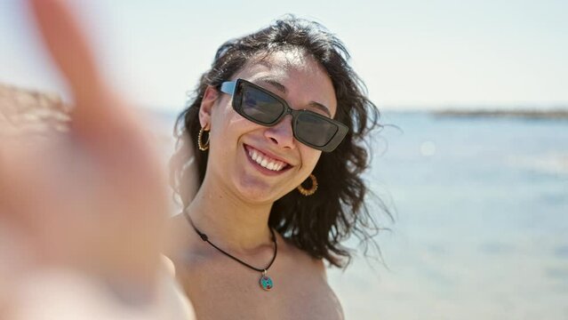 Young beautiful hispanic woman tourist smiling confident having video call kissing at beach