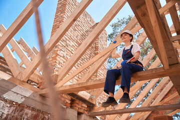 Woman roofer sitting on roof beam and enjoying done roofing works