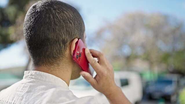 Young hispanic man speaking on the phone backwards at street