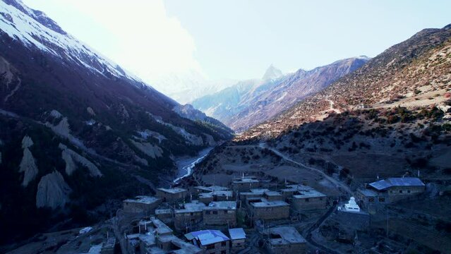 Aerial revealing backwards view colorful traditional nepals Khangshar village houses in Mamang district. Tilicho base camp trail with sunset background in Himalayas mountains.