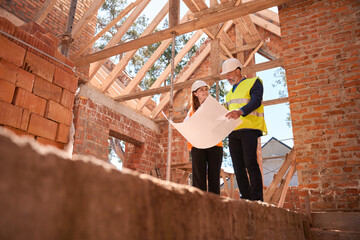 Female architect and male contractor discussing floor plan looking at project