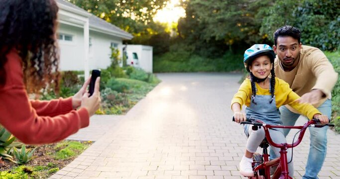 Mother, father and kid on bike learning in driveway with phone to record video, photograph or family support. Excited parents teaching happy girl on bicycle with mobile for memory, fun games and care