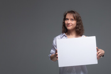 A young woman smiles and holds a white sheet in front of her on a gray background.