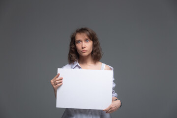 A young woman with bewildered face holds a white sheet in front of her on a gray background
