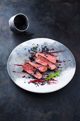 Gourmet barbecue dry aged angus roast beef steak with capers and rocket lettuce in amarena cherry sauce served as close-up in a Nordic design plate with copy space