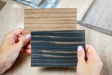 A woman is holding samples of different colors in her hands at the same time and choosing pieces of colored wood to choose a floor.