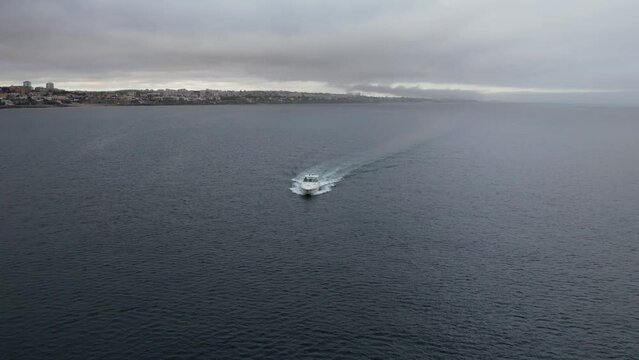 POV aerial drone view tracking a speeding yacht on a bay during a cloudy day - captured in Cascais, Portugal