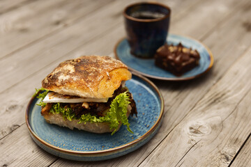 A sandwich with coffee and a pastry on blue plates standing on a wooden table.