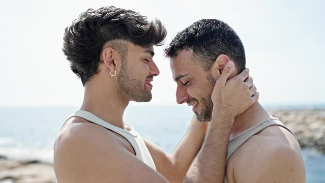 Two men couple standing together kissing at seaside