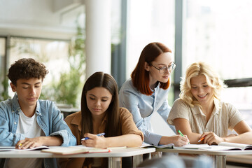 Young smiling teacher or tutor having lesson, assisting, explaining something, studying, learning language with school children sitting in classroom. Education concept 