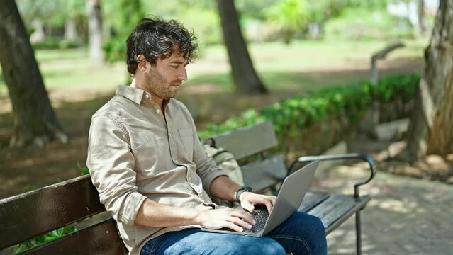 Young hispanic man using laptop sitting on bench at park